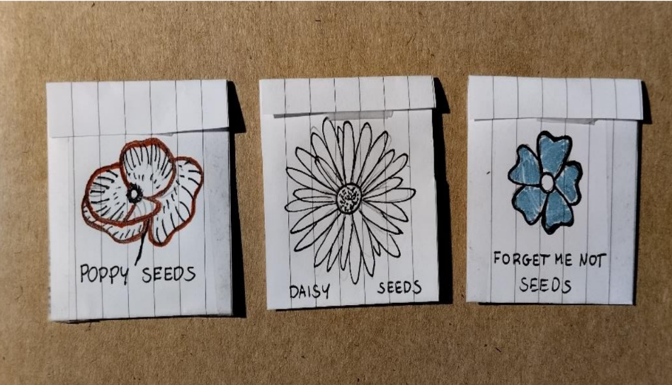 three paper envelopes that have drawings of flowers on them and have seeds inside 